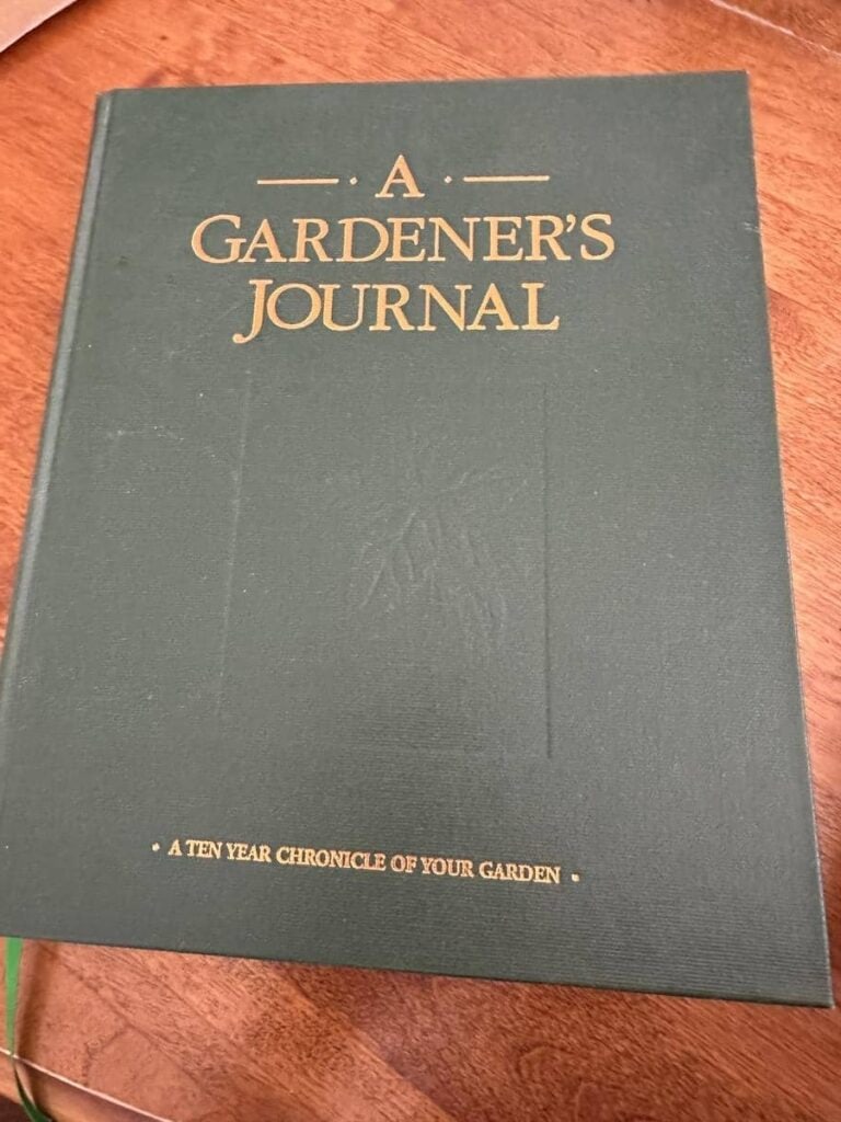 A hardcover journal titled A Gardener’s Journal: A Ten Year Chronicle of Your Garden lies on a wooden table. Keeping a long-term gardening log supports seasonal planning and helps beginners track what grows best in their evolving homestead gardens.